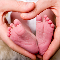 Två händer formar ett hjärta runt en bebis fötter.