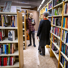 två personer samtalar vid bibliotekshyllor