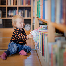 Barn i 2-årsåldern tar bok ur biblioteksbokhylla